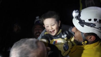 Syrisch jongetje lacht naar hulpverleners nadat hij gered is